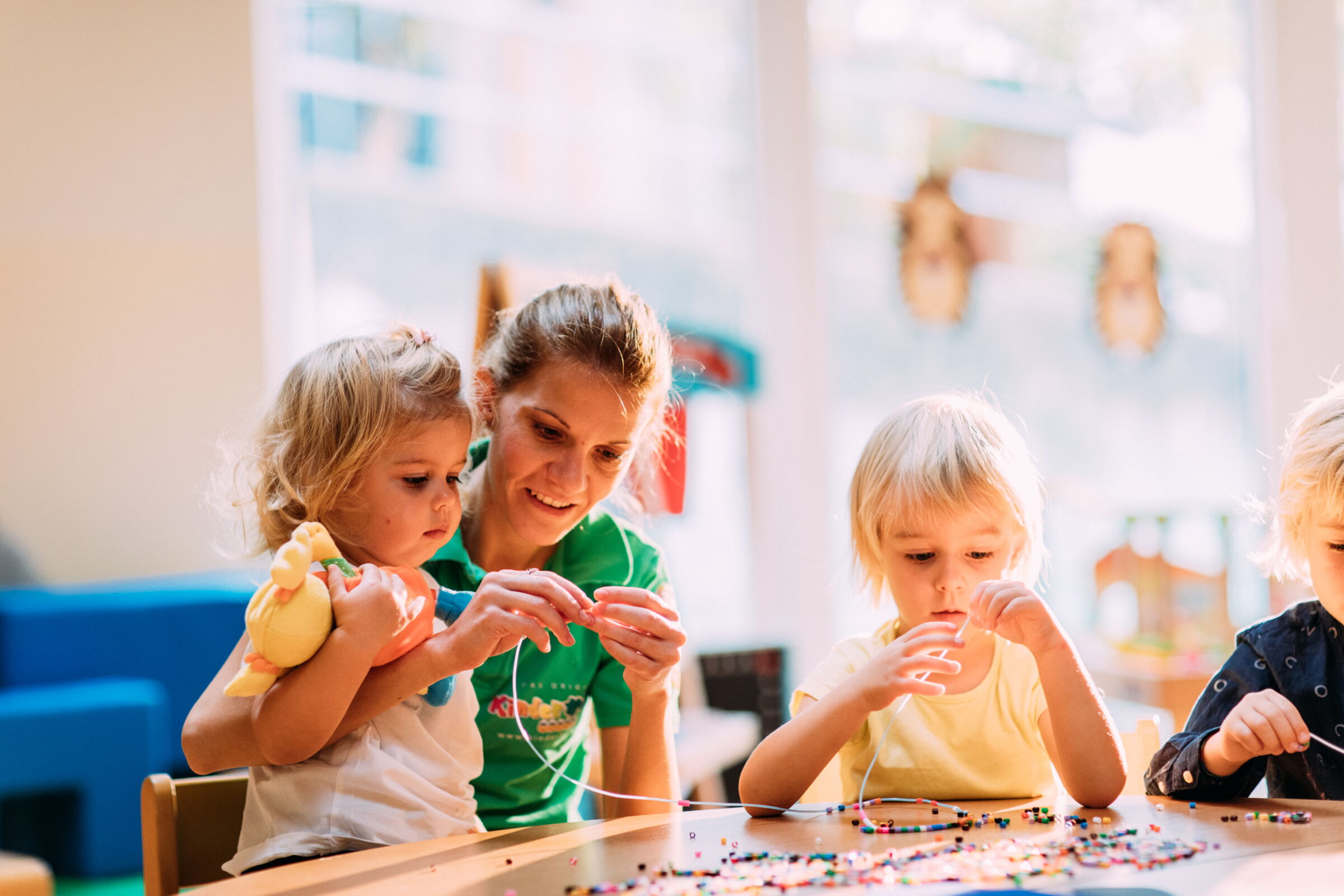 Kinder basteln mit einer Betreuerin, fröhliche Atmosphäre in heller Umgebung.