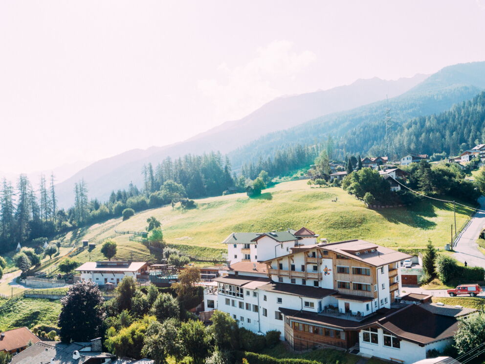Hotel in idyllischer Berglandschaft mit umliegenden grünen Wiesen und Bergen im Hintergrund.