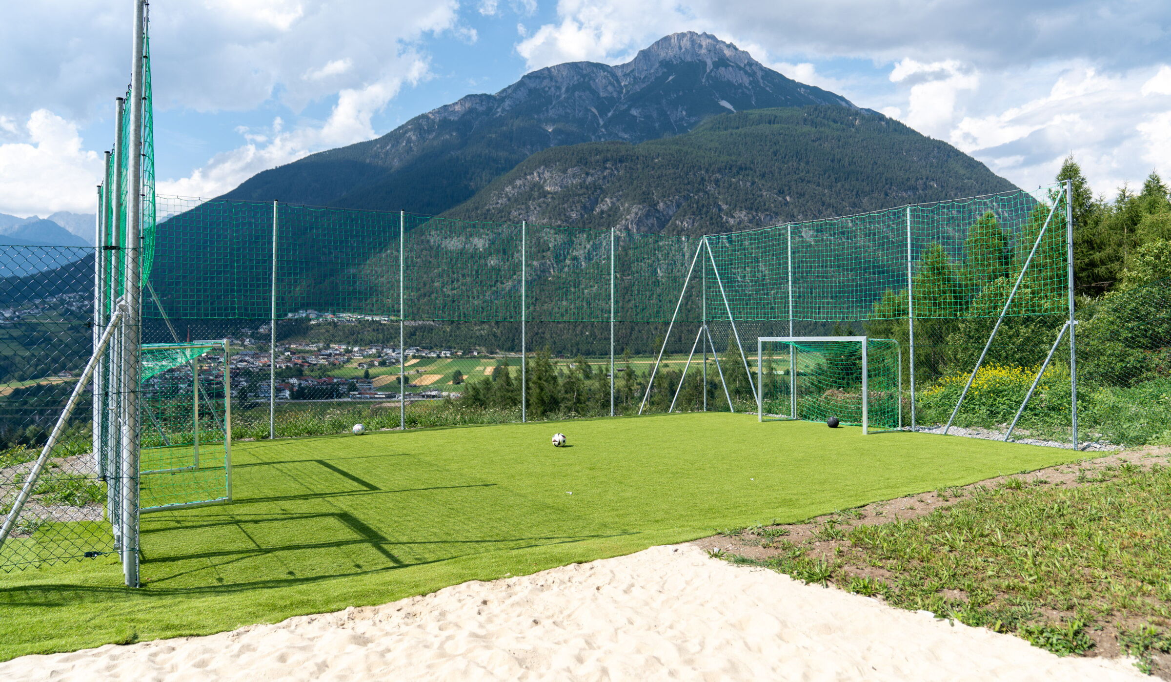 Fußballplatz mit Toren vor beeindruckendem Bergpanorama und grünem Tal