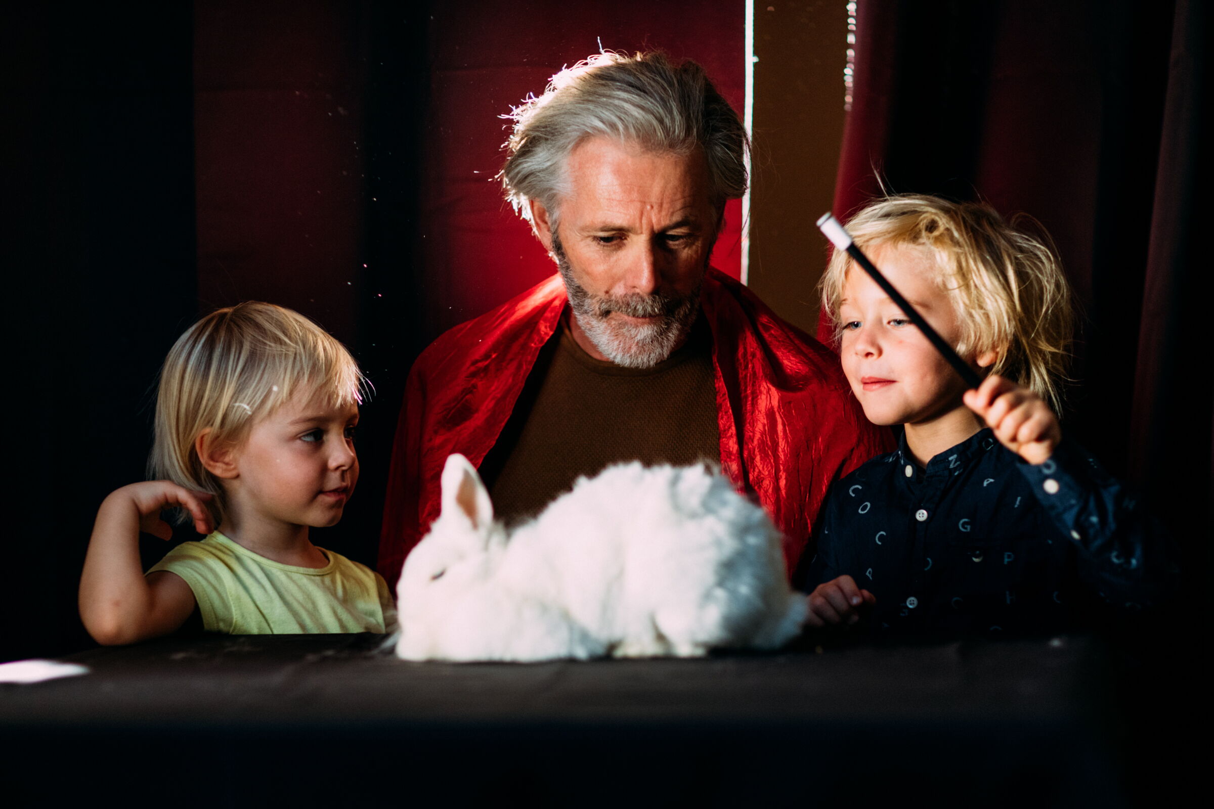 Two children and an elderly man with a rabbit and a magic wand.