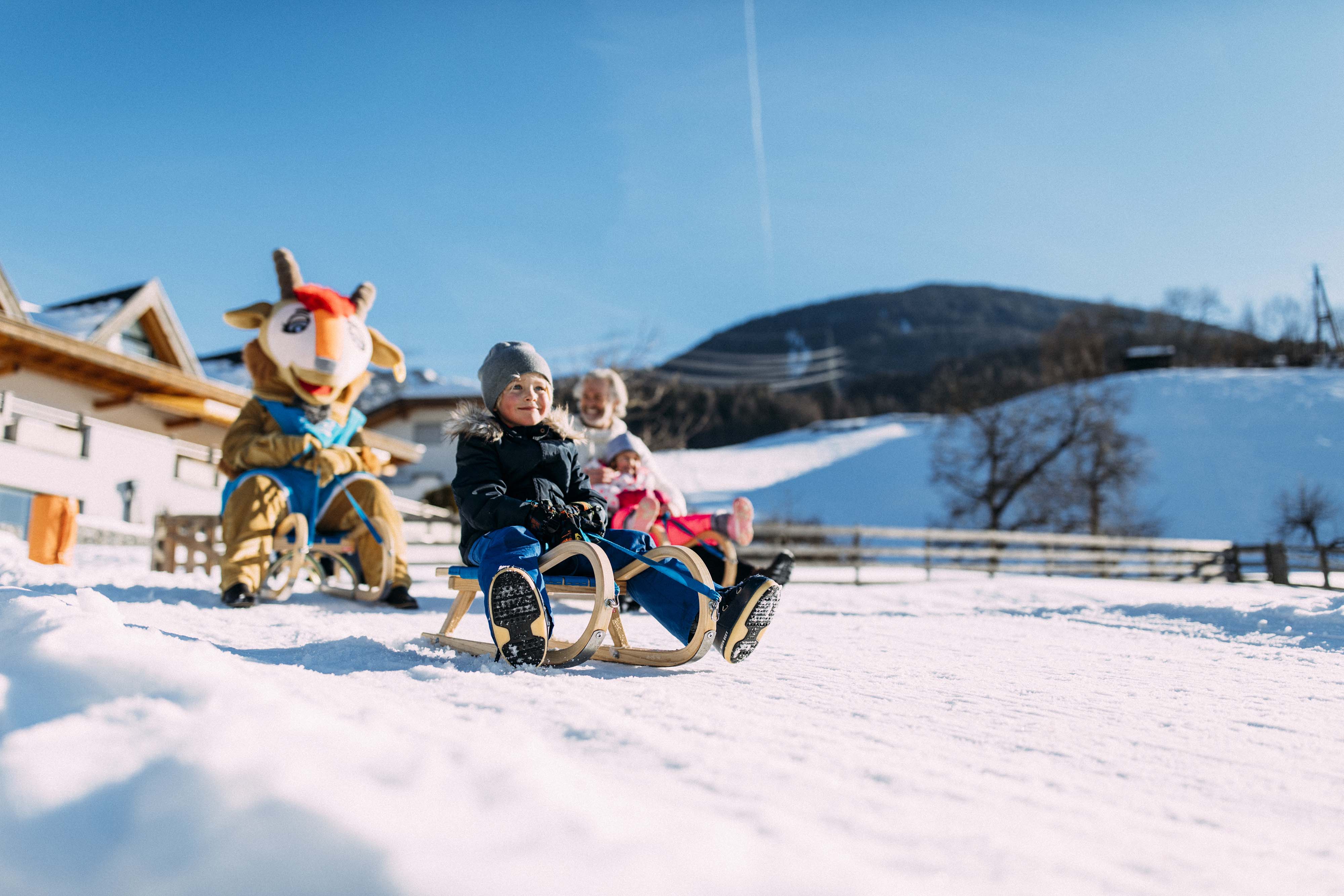 Kinder rodeln mit Pitzi-Maskottchen im verschneiten Pitztal