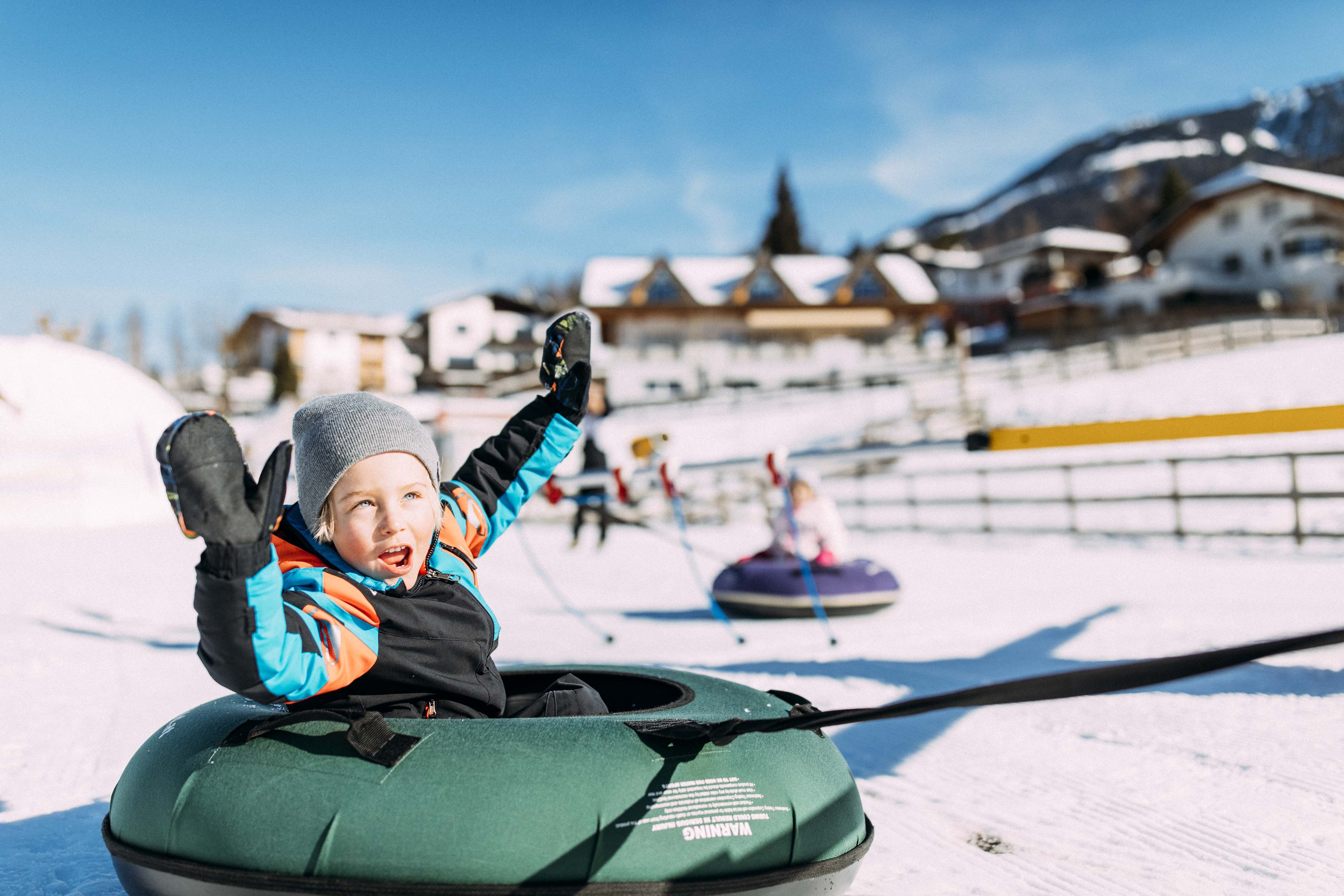 Kind genießt fröhliches Snowtubing im sonnigen Winterwunderland Tirol.